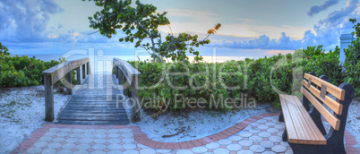 Bench overlooks a wooden boardwalk onto Naples Beach at sunset