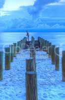 Fisherman stands on an old pier at the ocean on Naples Beach