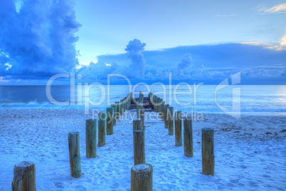 Old pier at dusk at the ocean on Naples Beach with dark skies ov