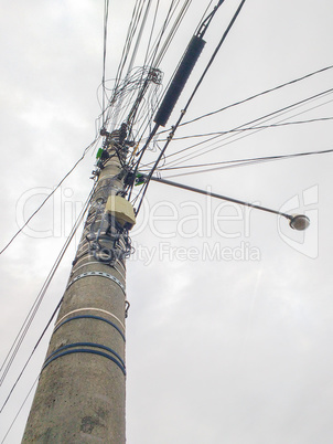 Concrete pole with electric wires and lamp with cloudy sky in the background