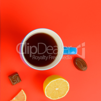Blue cup with tea , lemon slices and chocolate candies on a red