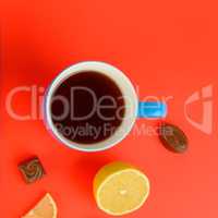 Blue cup with tea , lemon slices and chocolate candies on a red