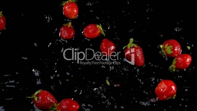 Strawberries falling on water on black background