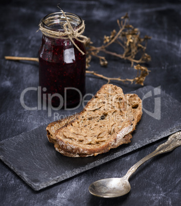 a piece of rye bread and a jar of raspberry jam