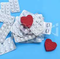 a stack of different pills in a package and two red hearts