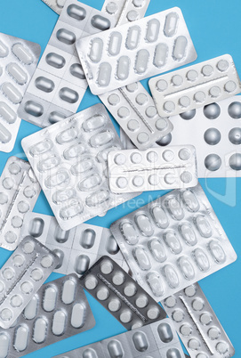 scattered various pills in gray packaging on a blue background