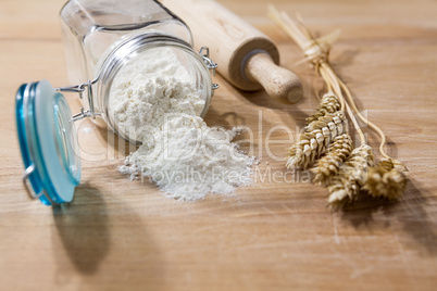 Flour in glass jar with rolling pin and sheaves of wheat