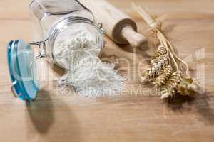 Flour in glass jar with rolling pin and sheaves of wheat