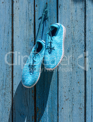 textile sneakers hang on a nail against the background of blue