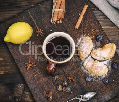 brown ceramic cup with black tea and croissants on a wooden boar