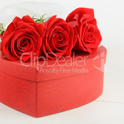 Gift box in the form of heart and scarlet roses on white wooden