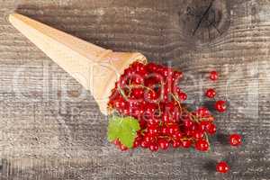 Red currant fruits in ice cream cone on wooden table