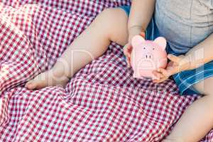 Baby Boy Sitting on Picnic Blanket Playing With Piggy Bank