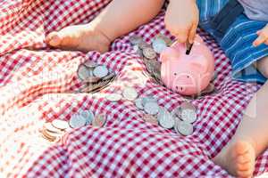 Baby Boy Sitting on Picnic Blanket PUtting Coins in Piggy Bank