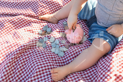 Baby Boy Sitting on Picnic Blanket PUtting Coins in Piggy Bank