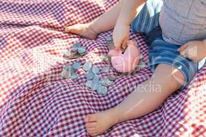 Baby Boy Sitting on Picnic Blanket PUtting Coins in Piggy Bank