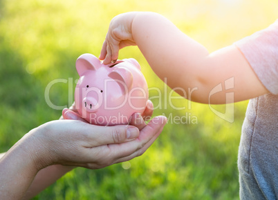 Woman Holds Piggy Bank While Baby Boy Puts Coins Inside