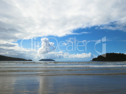 Beach with small waves on blue sky day and clouds.