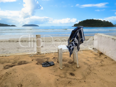 View of deserted beach with chair and towel.