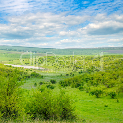 Green field and blue sky. Picturesque hills formed by an old riv