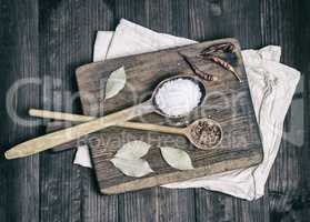 two wooden spoons with spices and white salt on a brown cutting