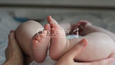 Baby feet in mother hands. Mother doing easy foot massage. Mother hold little baby legs and stroking it.