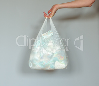 Woman hand holding a plastic bag full of dirty used baby diapers