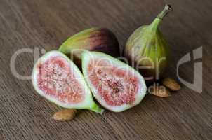 Close-up of fresh figs with one slised ripe fig and three almond nuts on a wooden table background