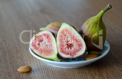 Close-up of fresh figs with one slised ripe fig and three almond nuts lying on white plate on a wooden table background