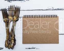notebook with brown empty pages and a pile of metal forks