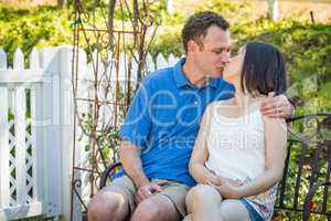 Young Caucasian Man and Chinese Woman Sitting On Bench Kissing