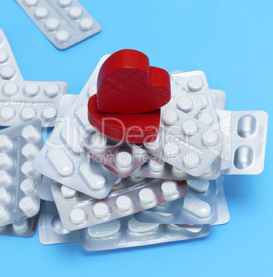 stack of different pills in a package and two red hearts