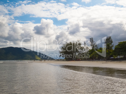 Sunny beach with green hills in the background.