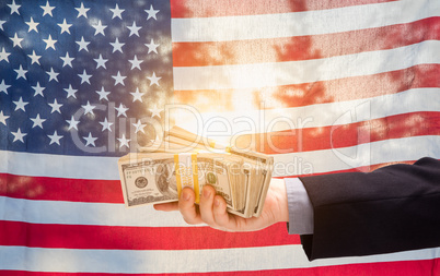 Hand Holding Stacks of Cash In Front of American Flag