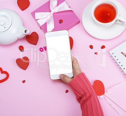right female hand in a pink sweater is holding a white smartphon