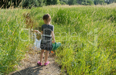 A girl with a toy frog is standing near a swamp