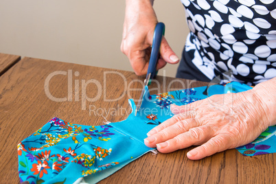 Elderly woman cuts out a piece of fabric for a dress