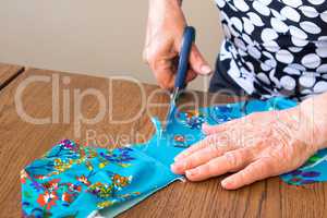 Elderly woman cuts out a piece of fabric for a dress