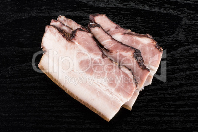 Fresh smoked english bacon on black wood