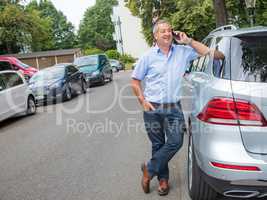 Man is standing in the street next to car and talking on the phone