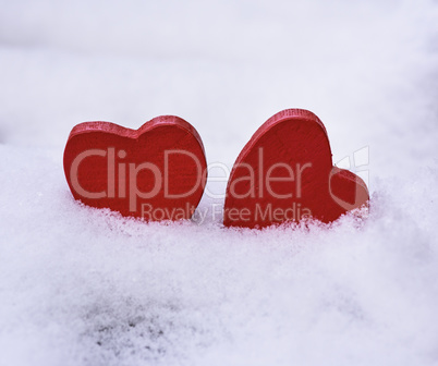two red wooden hearts lie on white snow