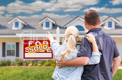 Young Adult Couple Facing and Pointing to Front of Sold Real Est