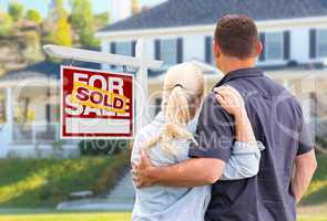 Young Adult Couple Facing Front of Sold Real Estate Sign and Hou