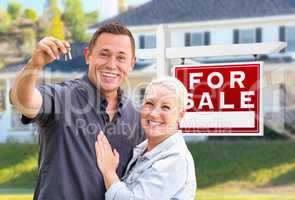 Young Adult Couple With House Keys In Front of Home and For Sale