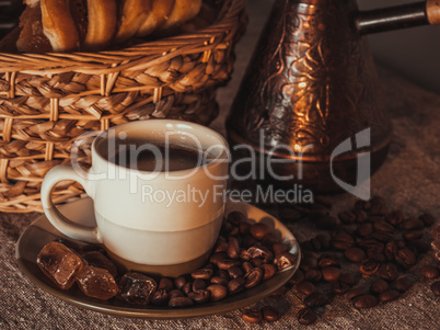 cup of coffee on textile with beans, dark candy sugar, pots, basket and cake