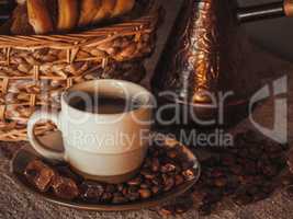 cup of coffee on textile with beans, dark candy sugar, pots, basket and cake