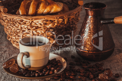 cup of coffee on textile with beans, dark candy sugar, pots, basket and cake