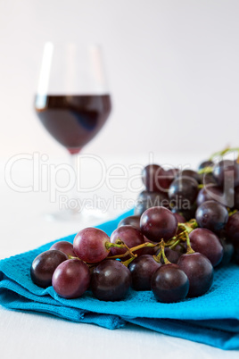 Closeup of a bunch of red grapes and a glass of red wine on back