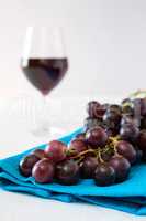 Closeup of a bunch of red grapes and a glass of red wine on back