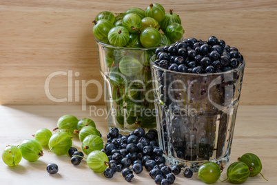 Blueberries and gooseberries in glass with scattered berries.